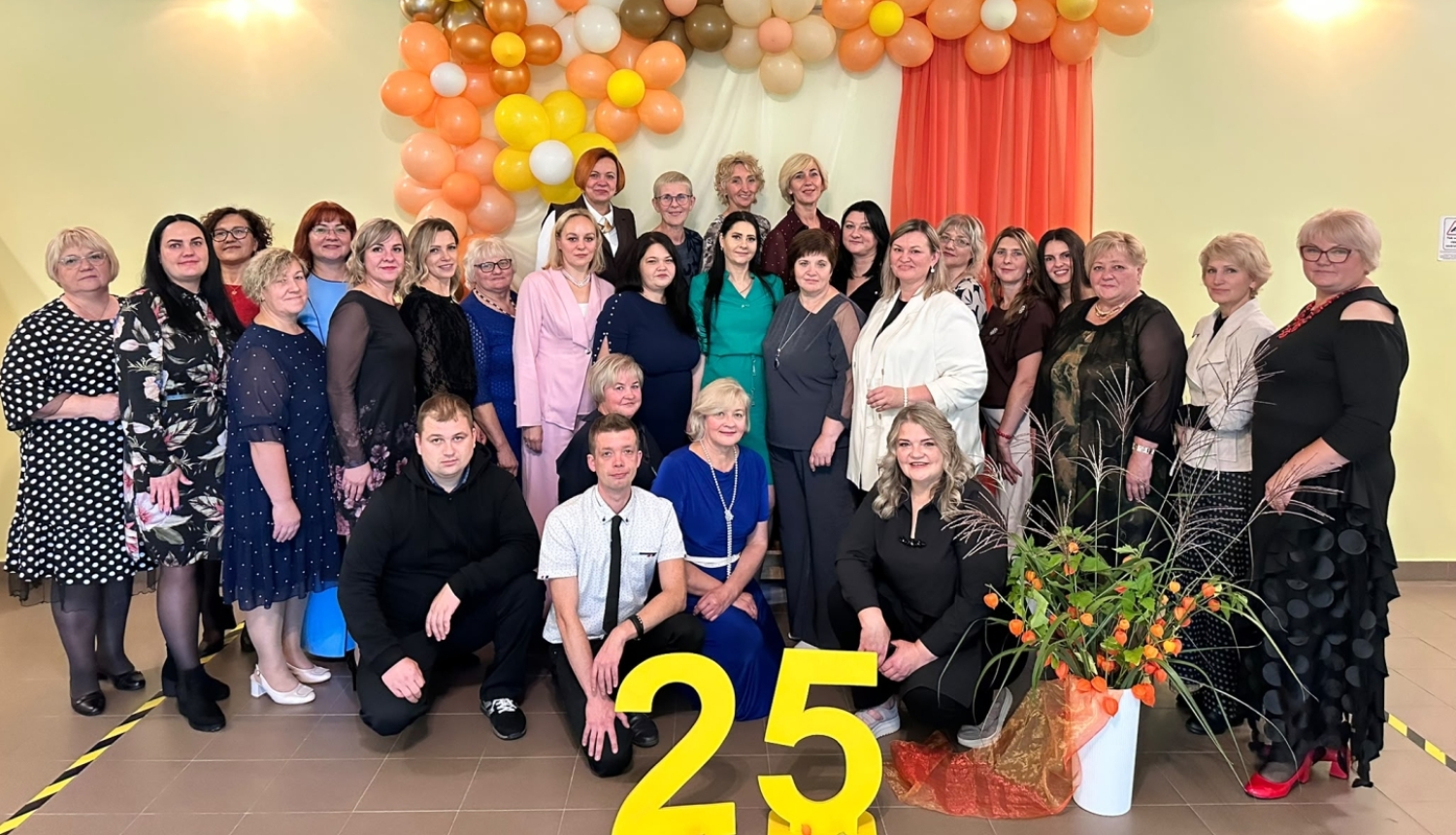 Cilvēki pozē pie svētku dekorācijām ar skaitli „25”