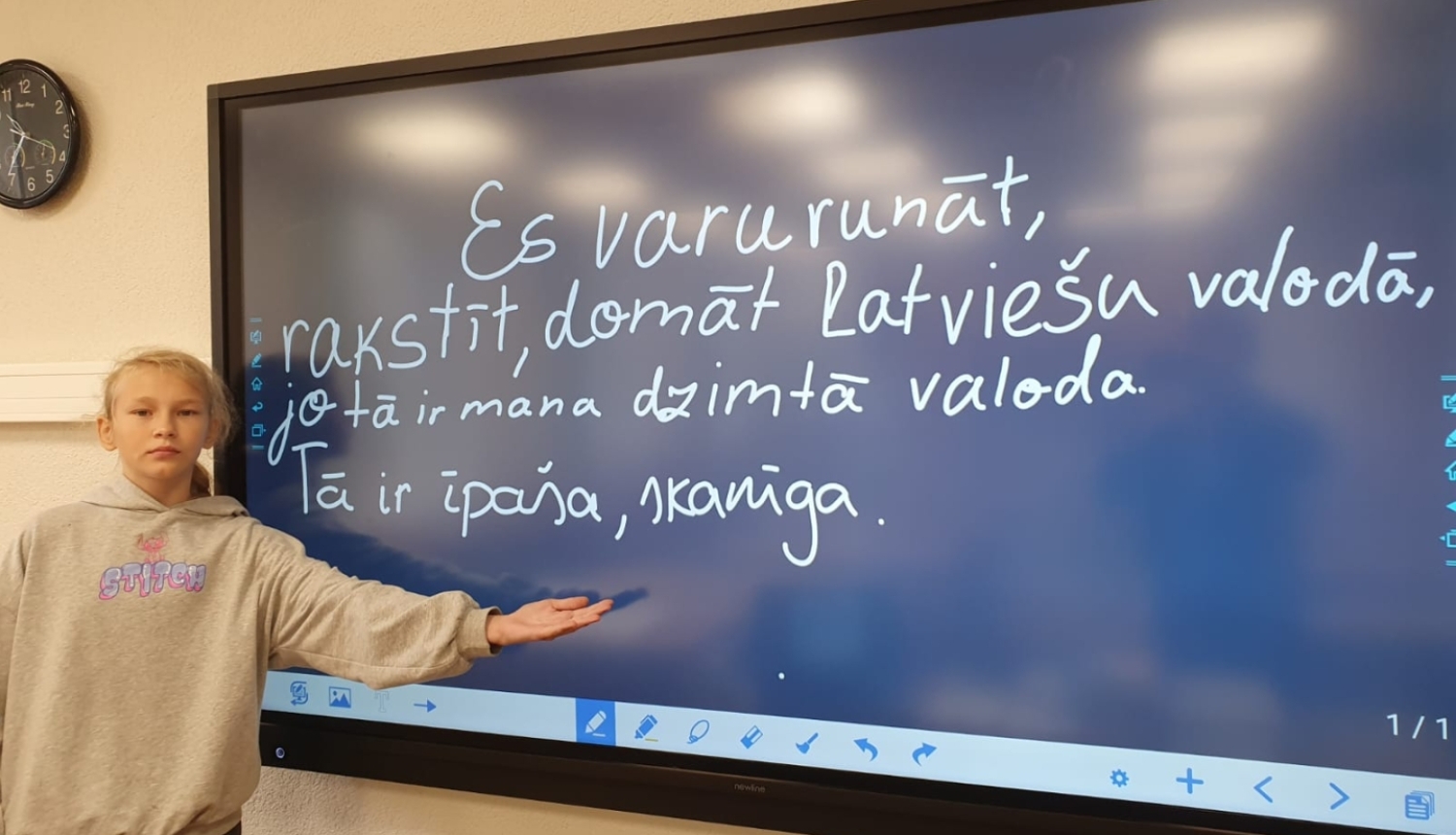 Skolniece pie interaktīvās tāfeles prezentē latviešu valodas uzdevumu