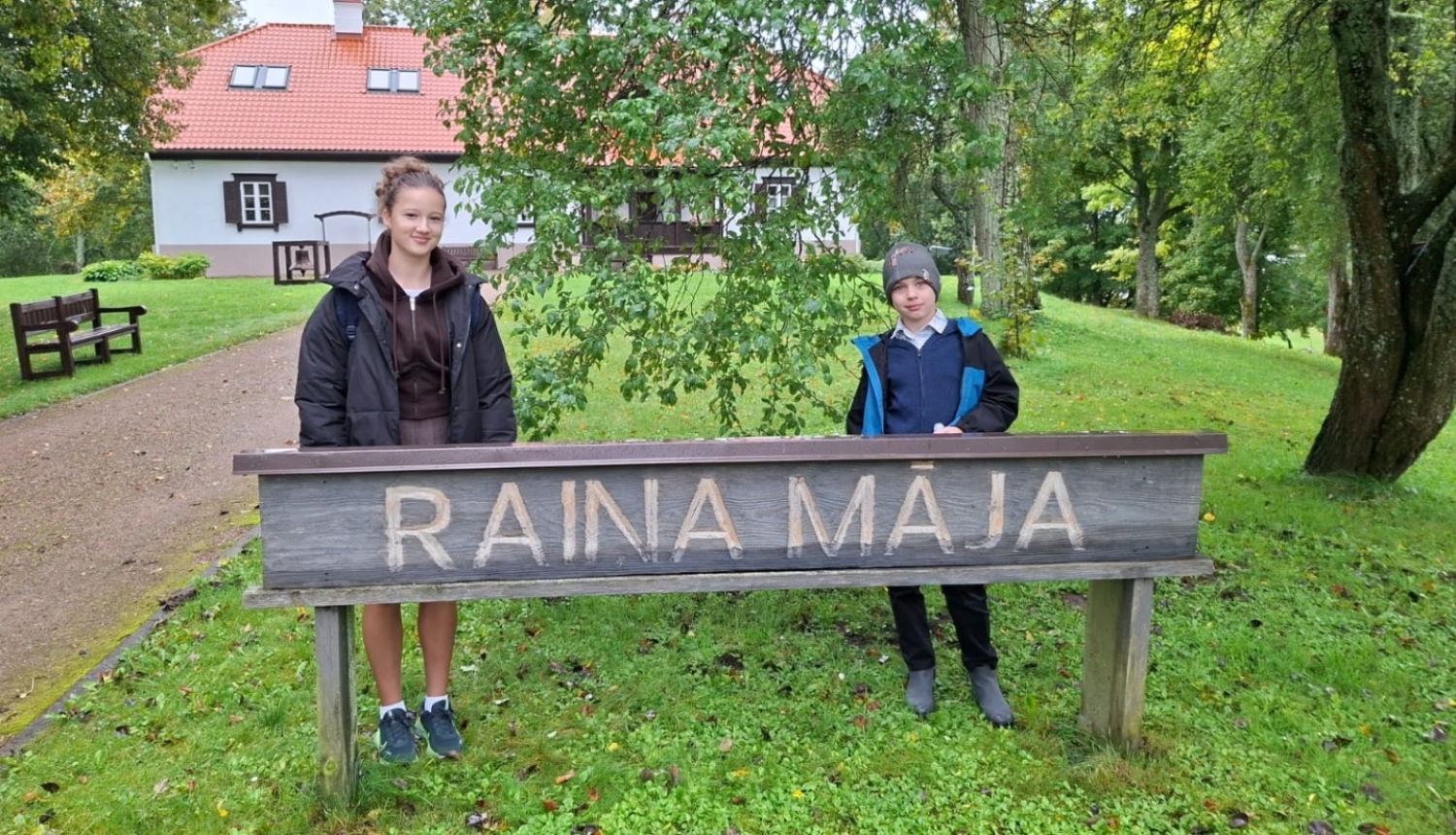 Divi skolēni pie „Raiņa mājas” zīmes