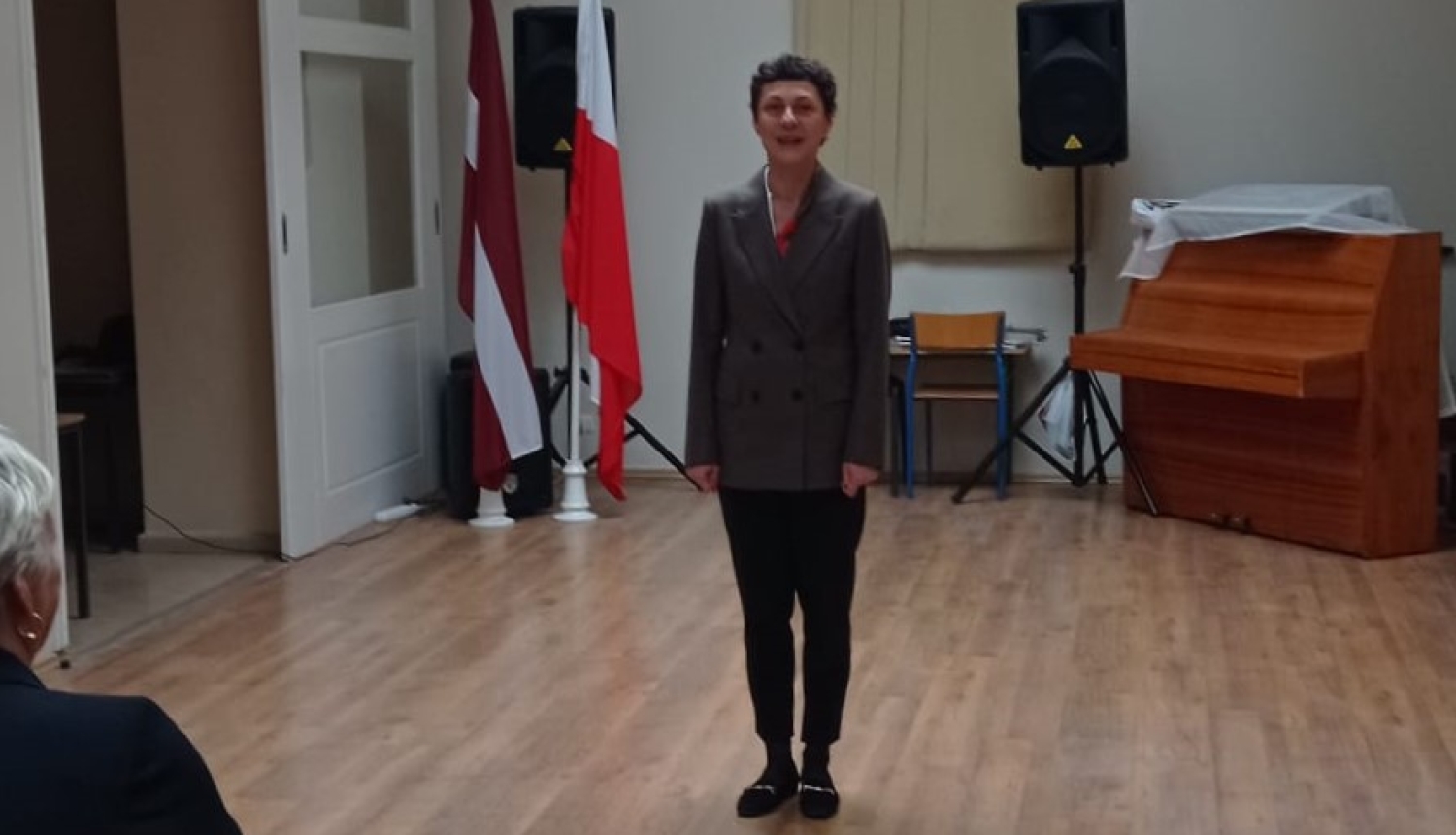 Cilvēks zālē pie Latvijas un Polijas karogiem