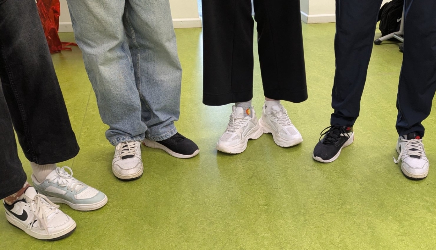 Skolēnu kājas un dažādi sporta apavi uz zaļas grīdas