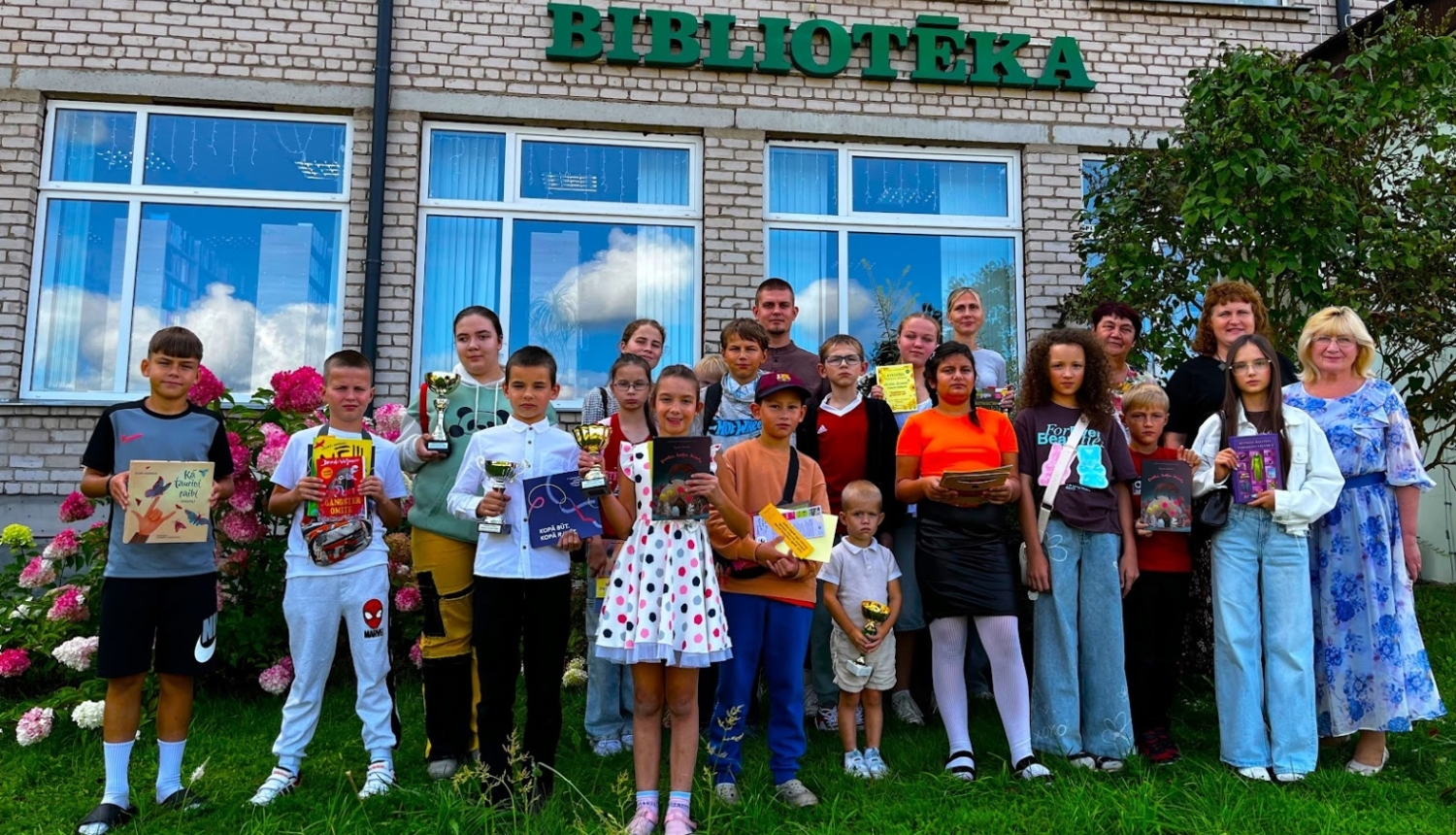 Bērni un pieaugušie pie bibliotēkas