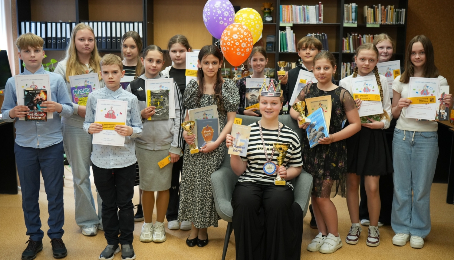Skolēni ar diplomiem, grāmatām un balvām bibliotēkā