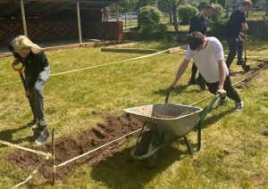 Cilvēki labiekārto zālienu, sagatavojot augsni volejbola laukuma izveidei