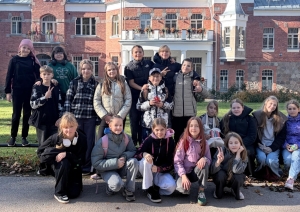 Skolēnu grupa pie vēsturiskas ķieģeļu muižas ēkas