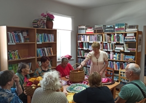 Cilvēku grupa bibliotēkā piedalās tamborēšanas paklāju meistarklasē