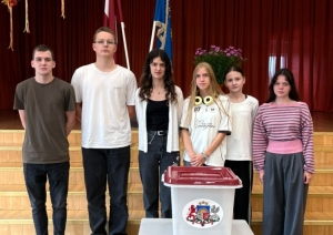 Seši jaunieši pie vēlēšanu urnas skolas zālē