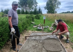 Divi cilvēki būvē un izlīdzina betona pamatus dārzā