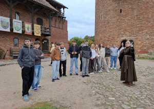 Skolēnu grupa kopā ar gidi viduslaiku pils pagalmā