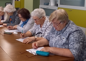 Seniori sēž pie galda un pilda rakstisku uzdevumu