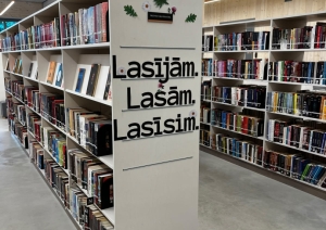 Plaša bibliotēkas grāmatu zona ar plauktiem un uzrakstu “Lasījām. Lasām. Lasīsim.”