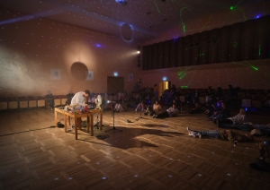 Elektroniskās mūzikas performance koncertzālē ar sēdošu un guļošu auditoriju