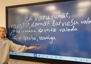 Skolniece pie interaktīvās tāfeles prezentē latviešu valodas uzdevumu