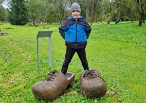 Skolēns pozē dārzā pie lieliem koka apaviem