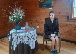 Skolniece sēž Raiņa mājas koka interjerā pie galda