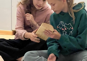 Divas skolnieces kopīgi pēta koka priekšmetu