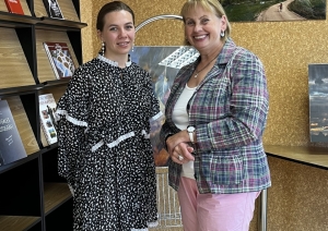 Divas sievietes smaida un pozē kopā izstādes telpā