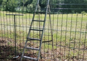 Metāla kāpnes pie zaļa žoga