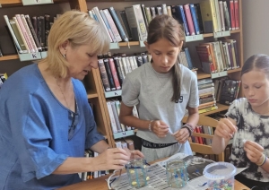 Bibliotekāre kopā ar divām meitenēm veido lukturīšus