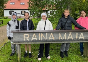 Pieci bērni stāv pie koka norādes „Raiņa Māja”