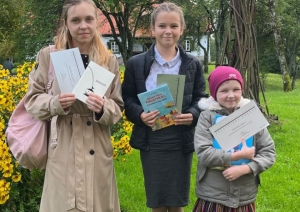 Trīs meitenes dārzā rāda grāmatas un diplomus
