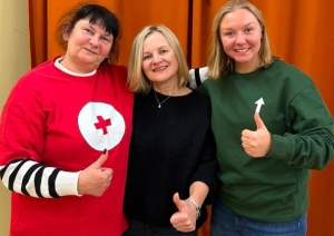 Trīs sievietes pozē fotogrāfijai pie oranža aizkara