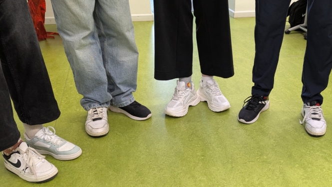 Skolēnu kājas un dažādi sporta apavi uz zaļas grīdas